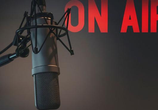 A recording booth microphone with the words "ON AIR" projected on the wall of a studio