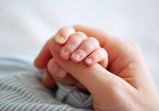 A close up of an adult grasping the hand of an infant