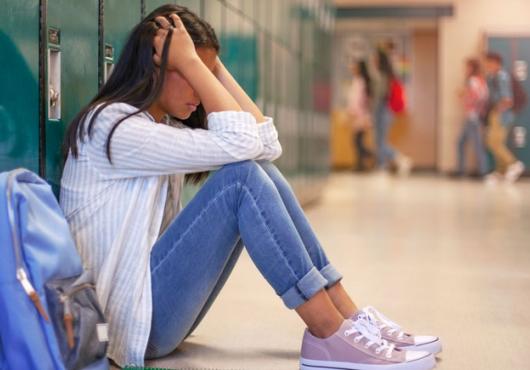 Image of a female high school student sitting on the floor by her locker, head in hands