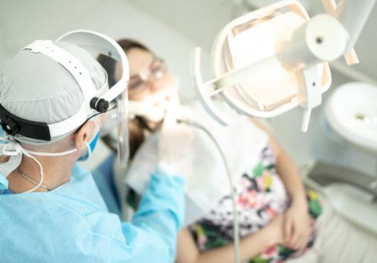 Dentist in full PPE with his hands inside a female patient's open mouth