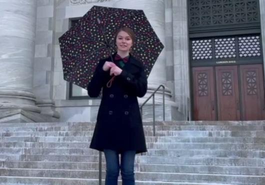 A women holding a polkadot umbrella stands in front of Gordon Hall