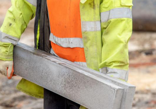 Photo of a construction worker carrying a large concrete beam 