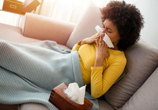 A sick person blowing their nose on a couch