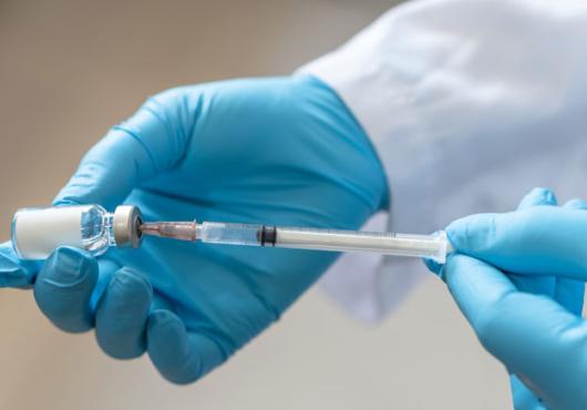 Blue-gloved hands holding a vaccine syringe