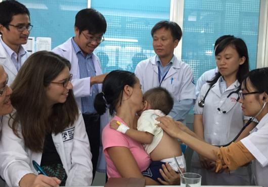 Group of medical students in Vietnam looking on as a baby is examined in clinic, held it its mother's arms.