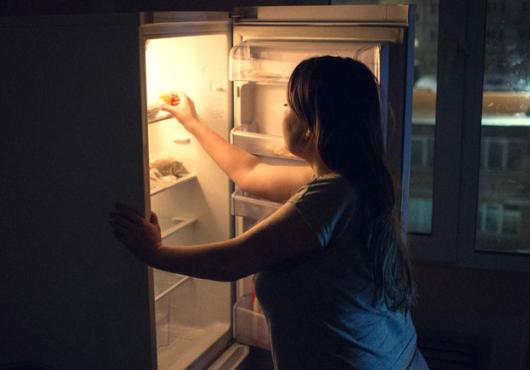 Photo image of woman getting something out of the refrigerator late at night