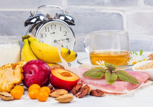 Photo of a bunch of fruit and food with an alarm clock nearby