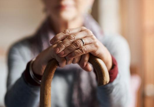 An out-of-focus person with their hands on top of a cane in focus in front of them