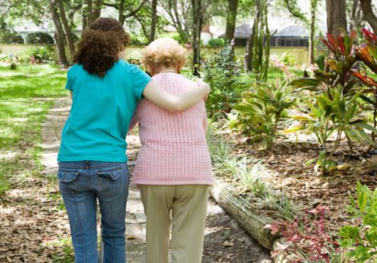 Caregiver walking with elderly woman, photographed from behind 