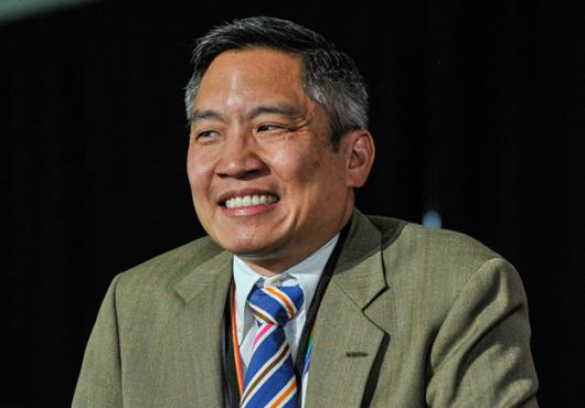 Photo of Bernard Chang with a green suit jacket and striped tie, smiling.