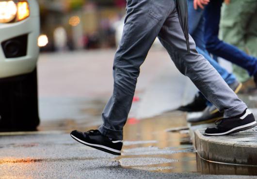 The lower half of a person stepping off a curb to cross the street in front of a car