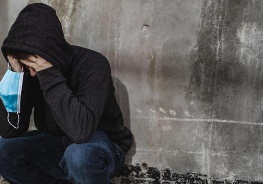 Person with a hoodie on holding their face in their hands and also a mask