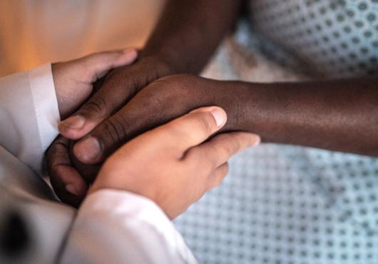 Image of a doctor's hands holding a black hospital patient's hands.  No faces.