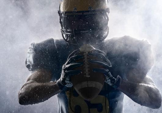 American football player in silhouette gripping a football. 