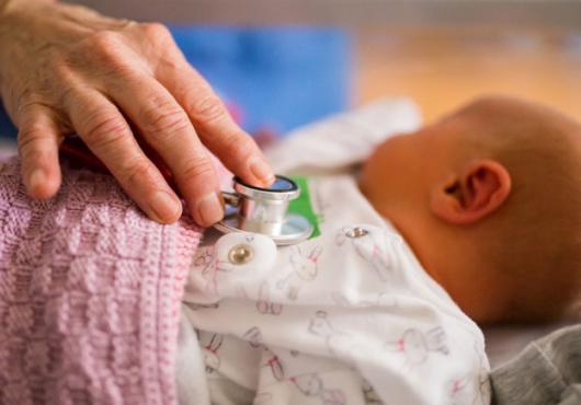 Photo of a hand with a stethoscope on a newborn baby's chest 