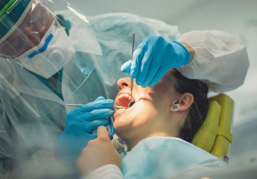 Dentist in full PPE with his hands inside a female patient's open mouth