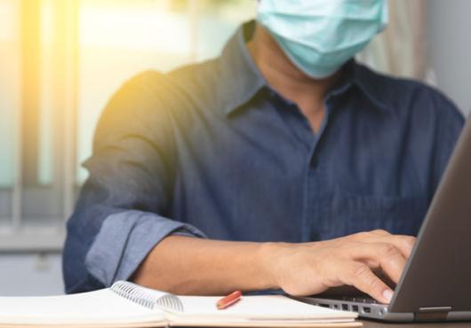 Guy with a mask typing on a laptop computer 