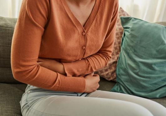 The torso of a sitting person hunched over with their arms wrapped across their stomach