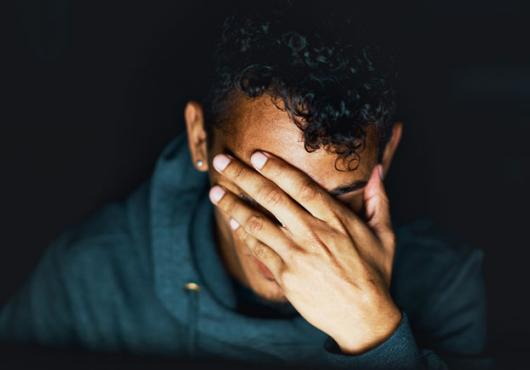 A close up of a person with their hand covering their face against a black background