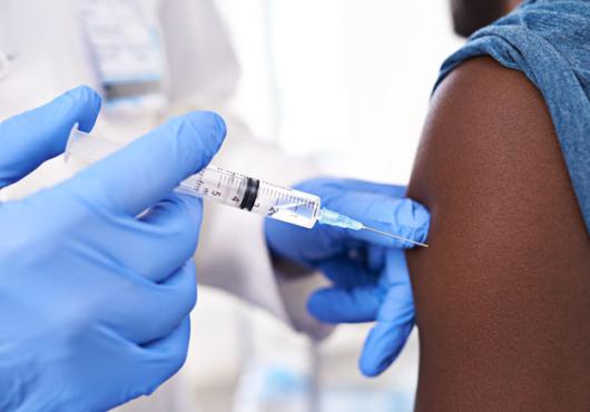 A closeup of a gloved healthcare provider injecting a vaccine into a patient's arm