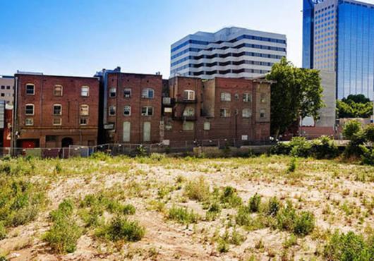 Urban settings showing older low brick housing structures wedged between an empty dirt lot and modern glass-sided high rise structures