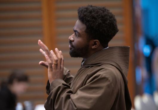 A man in a monk's habit speaks to an audience.