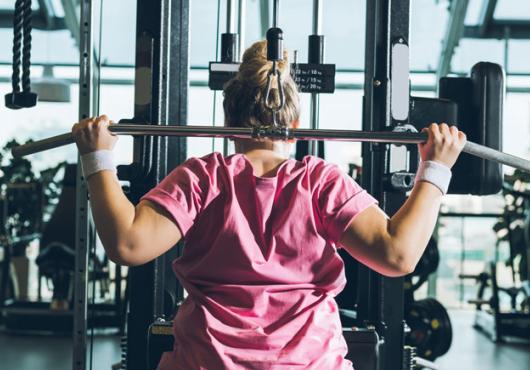 Photo of woman in pink top lifting weights in a gym