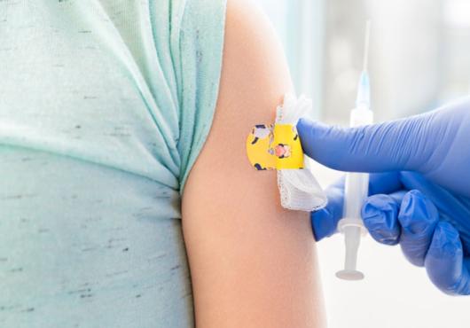 Photo of a child's torso with a bandaid on the arm and a blue glove with syringe
