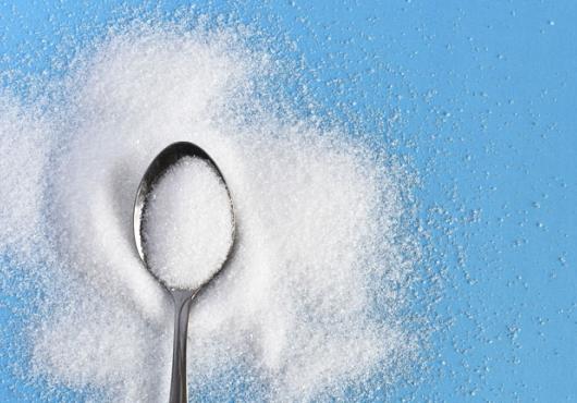 Photo of a spoon of sugar against a blue background