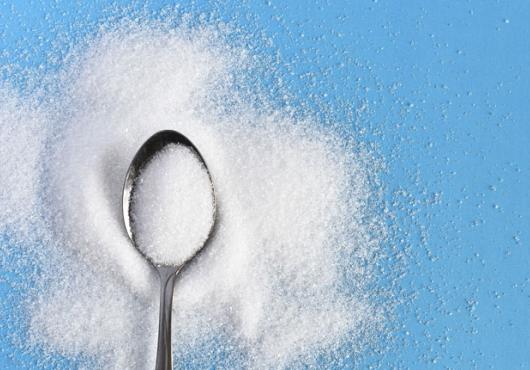 Photo of a spoon with sugar all around it against a blue background 
