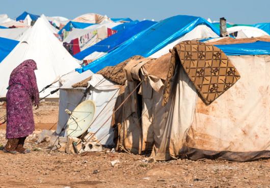 Image of a woman outside a makeshift tent in a Syrian refugee camp