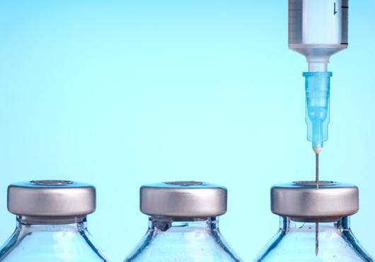 Image of 3 vaccine bottles and a syringe needle 