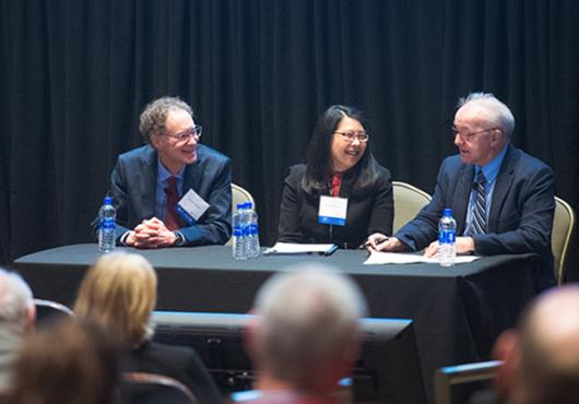 Three people at table in front of audience