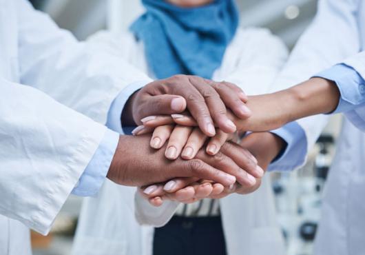 Close up of the stacked hands of three physicians with different ethnicities in solidarity.