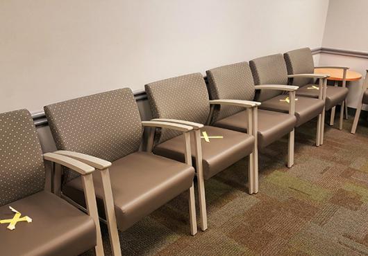 Empty chairs in waiting room, marked with X's for social distancing