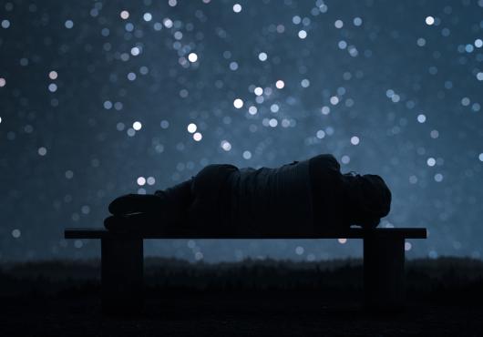Photo illustration of a sleeping female form in silhouette with a backdrop of a night sky and stars
