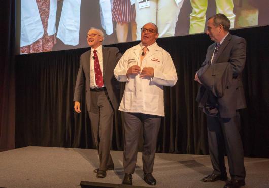 Alex Blavatnick (center) receives the gift of an HMS white coat from HMS Dean George Daley (left) and Harvard President Larry Bacow. 