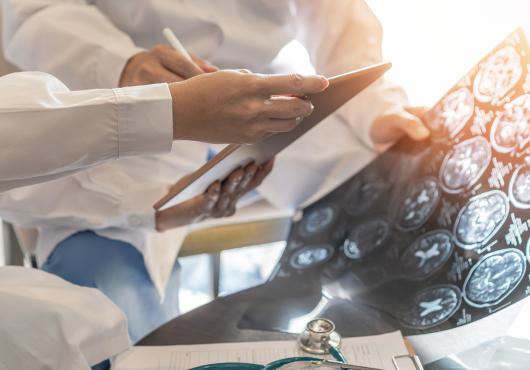 Closeup of the hands of two people wearing white lab coats examining medical images of a patient’s brain.