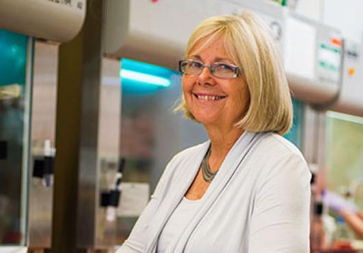 Smiling woman in white suit sitting at an angle in front of lab equipment