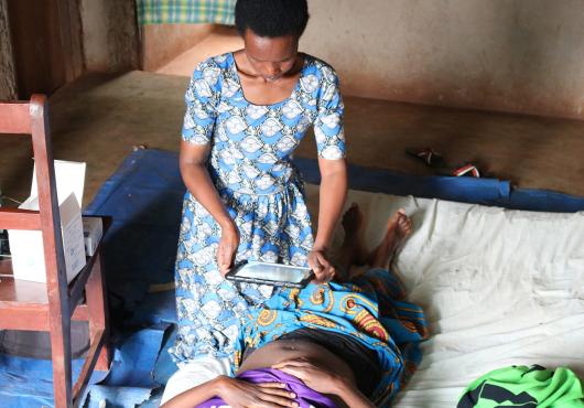 A female health care worker uses a tablet computer to take a photo of a woman lying on a bed