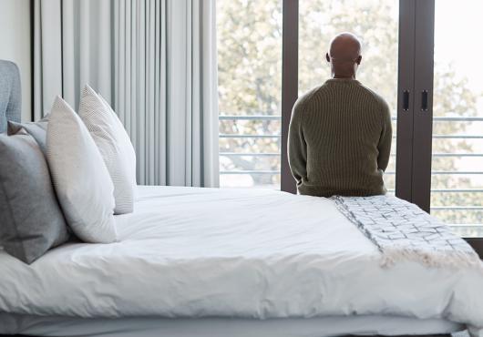 Rearview shot of a mature man looking through a window in a bedroom.