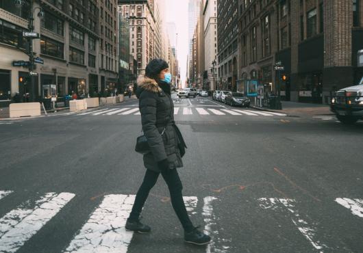 A woman in a surgical mask crossing a street in mid-town Manhattan