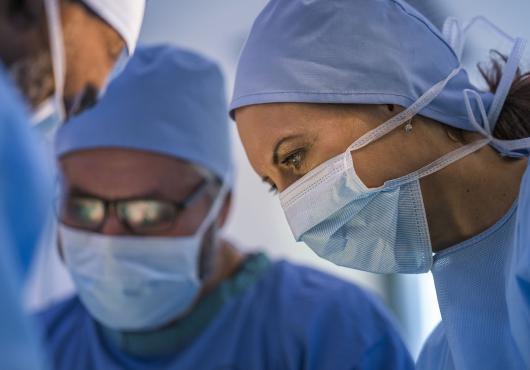 A woman in a surgical mask with men in surgical masks out of focus in the background.