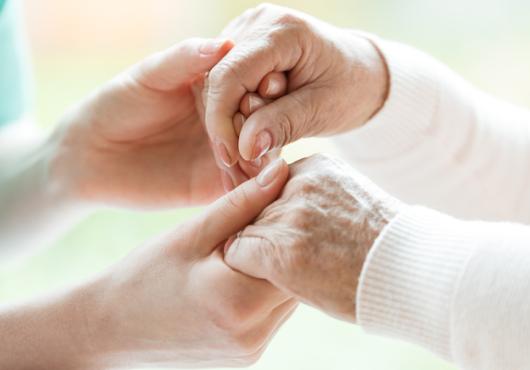Image: a caregiver holding hands with a hospice patient