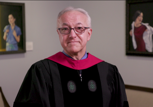Dean Daley, wearing academic regalia, speaking in Gordon Hall