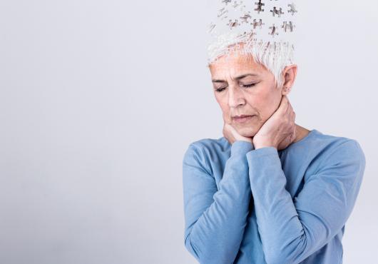 Photo of a distressed woman with short gray hair with illustration puzzle pieces flying out of the top of her head