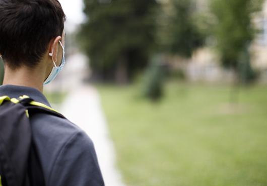 Rear view of a child with backpack and mask on facing a schoolyard