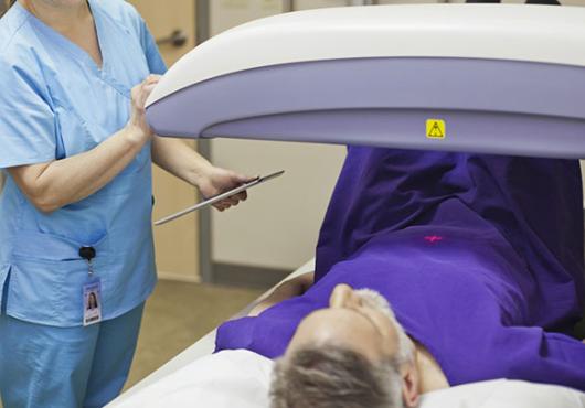 Photo of a gray-haired man lying on an exam table while a technician adjusts a scanning machine over him