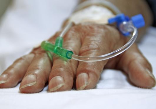 Photo of a surgery patient's hand resting on a bed, with tubes going into the hand