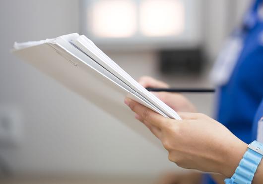 two people in scrubs, heads not shown, review a sheaf of papers indicating a patient file
